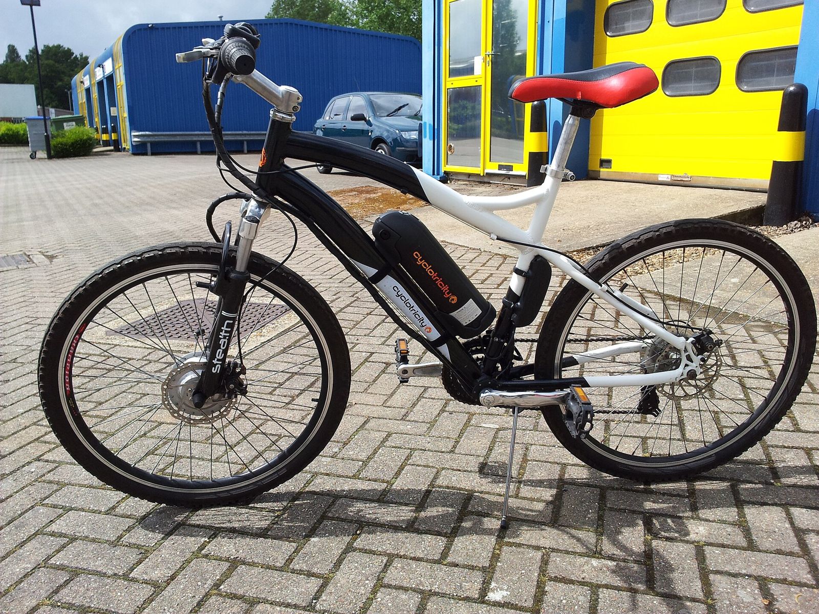Black and white bicycle with a front hub motor and a downtube battery, parked on paving.